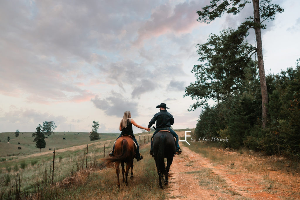 cowboy couple riding down dirt road holding hands