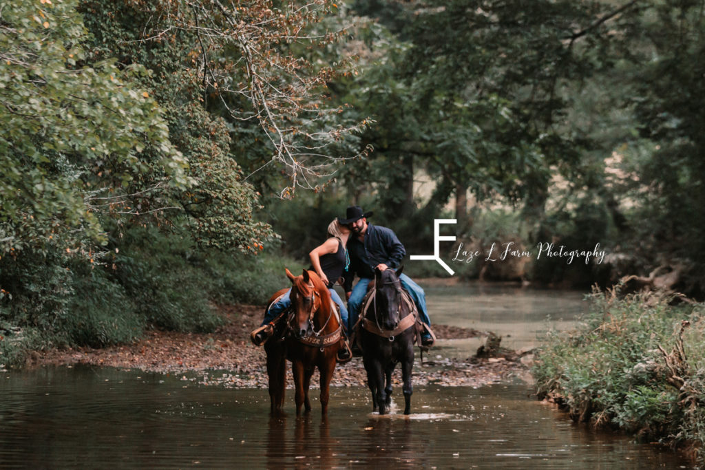 cowgirl kissing cowboy on cheek in creek on horseback