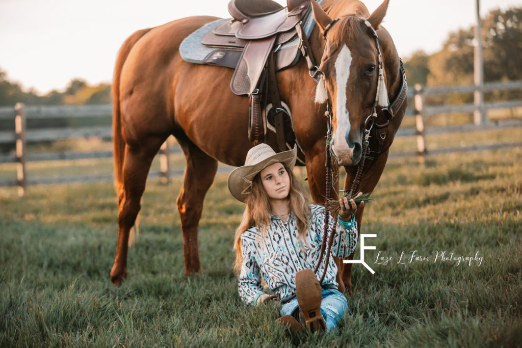 cowgirl sitting leaning on horse feeding it grass