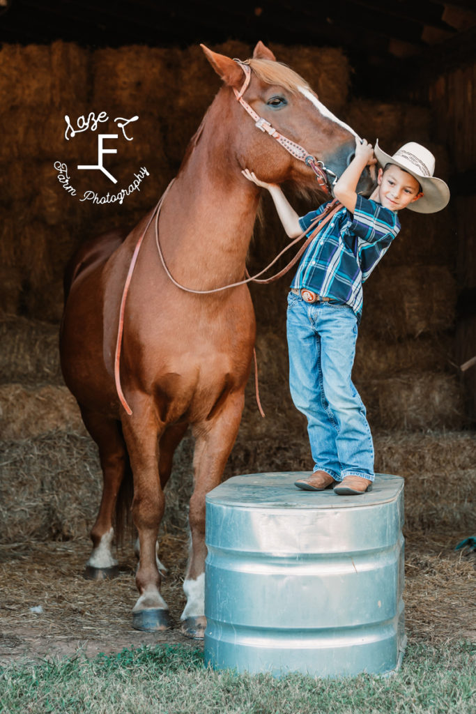 little cowboy standing on water trough with horse