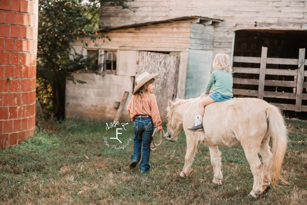 little cowgirl leading little sister around on pony