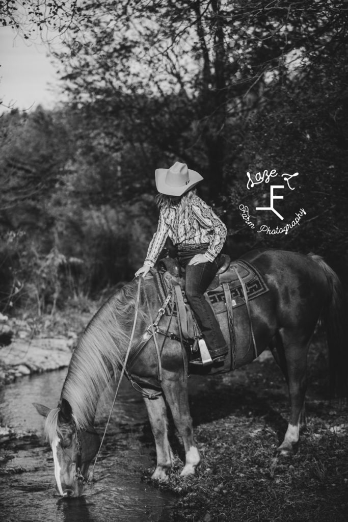 cowgirl letting horse drink in black and white