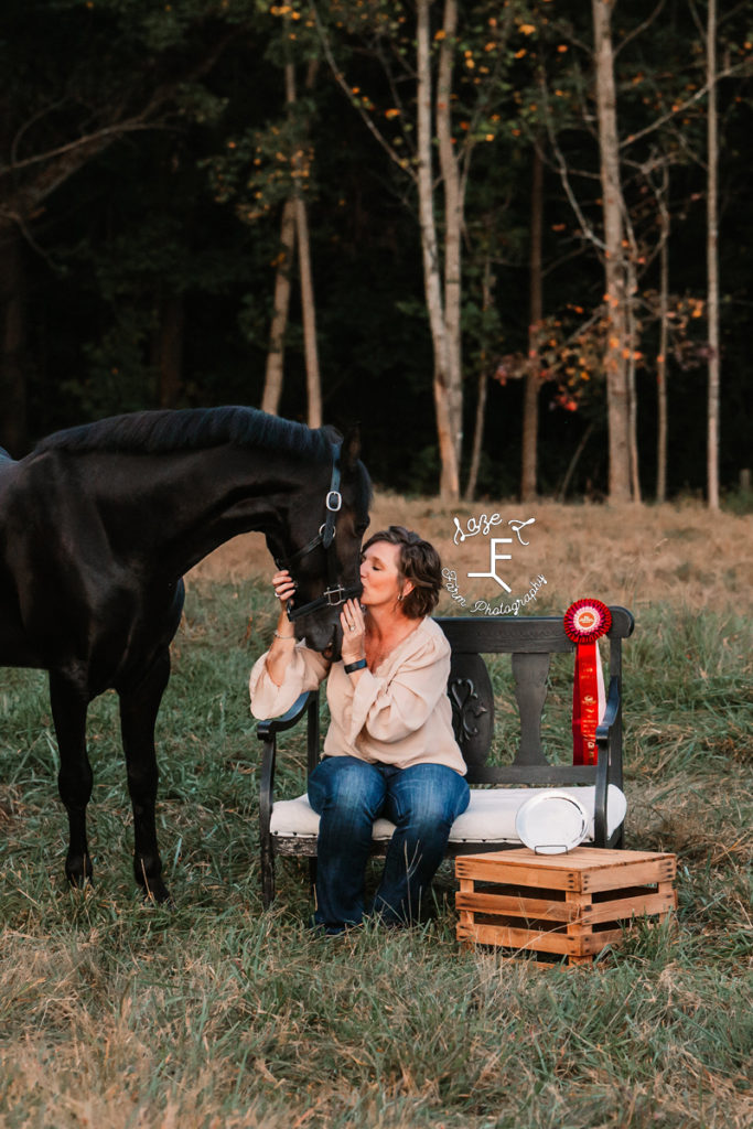 lady sitting kissing horse's nose with champ ribbon