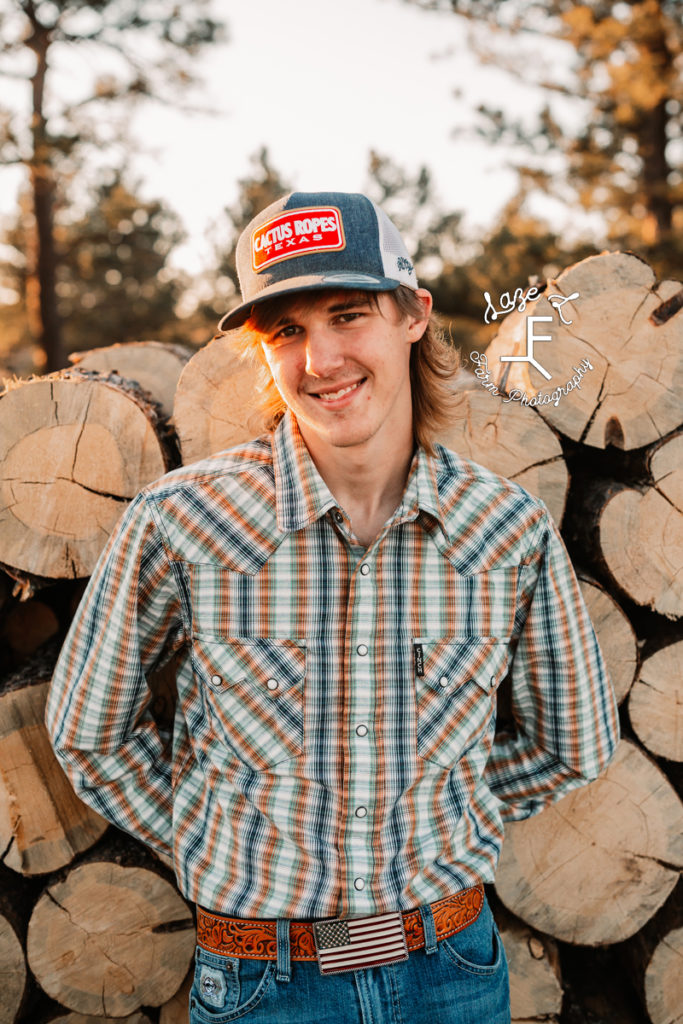 young guy in a hat in front of wood pile