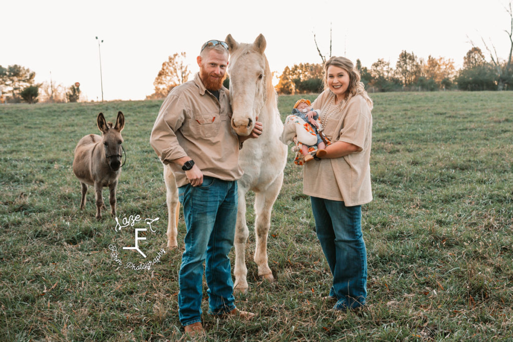 mom holding baby with dad, horse and mini donkey