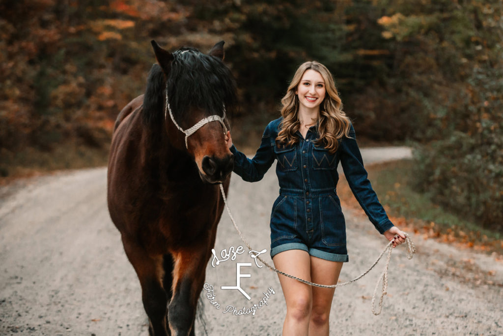 senior girl in blue jean romper walking shire cross horse