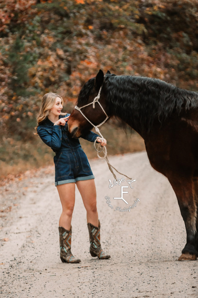 senior girl in romper pointing at horses nose