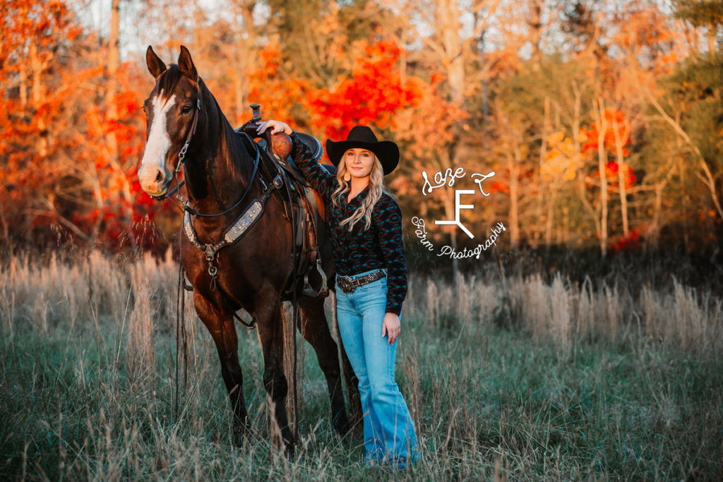 cowgirl standing with horse in fall colors