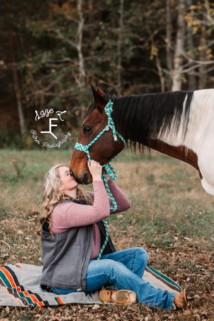 blond girl sitting kissing paint horse