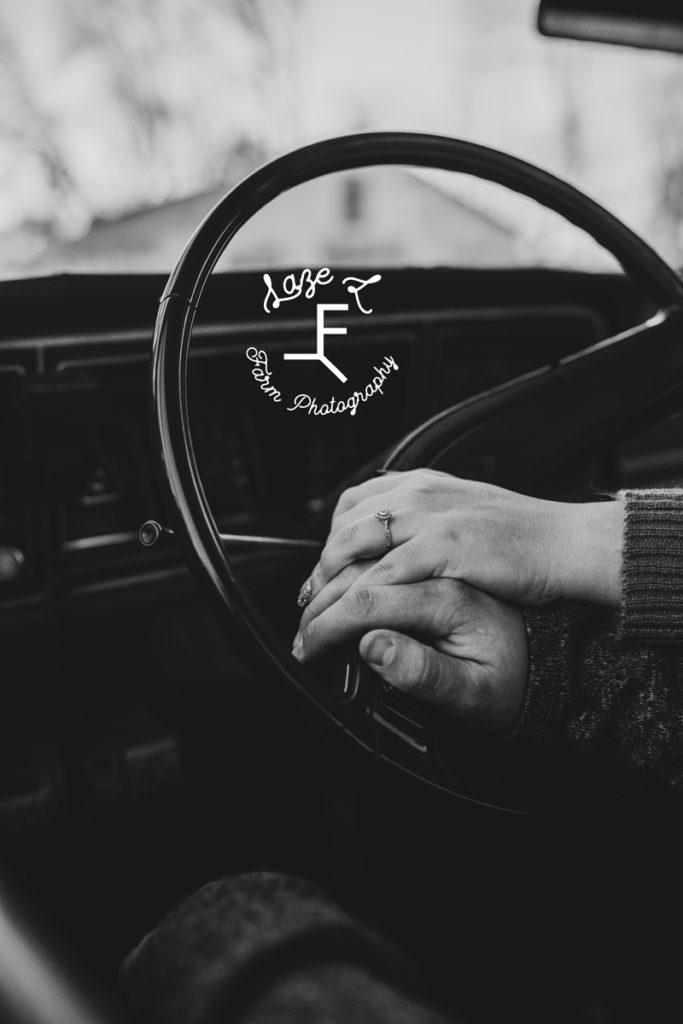 couple holding hands on steering wheel in black and white