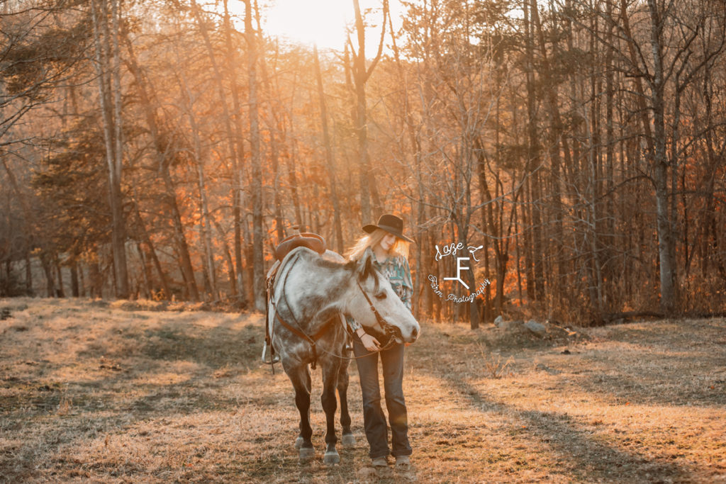 cowgirl with gray horse at sunset