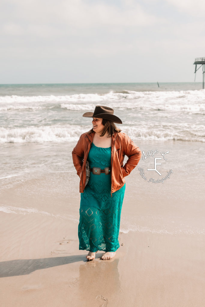cowgirl in teal dress walking away from ocean