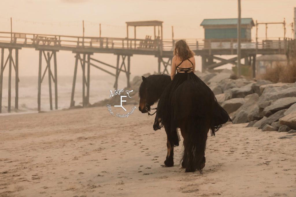 girl in black dress riding shire horse at sunset on beach