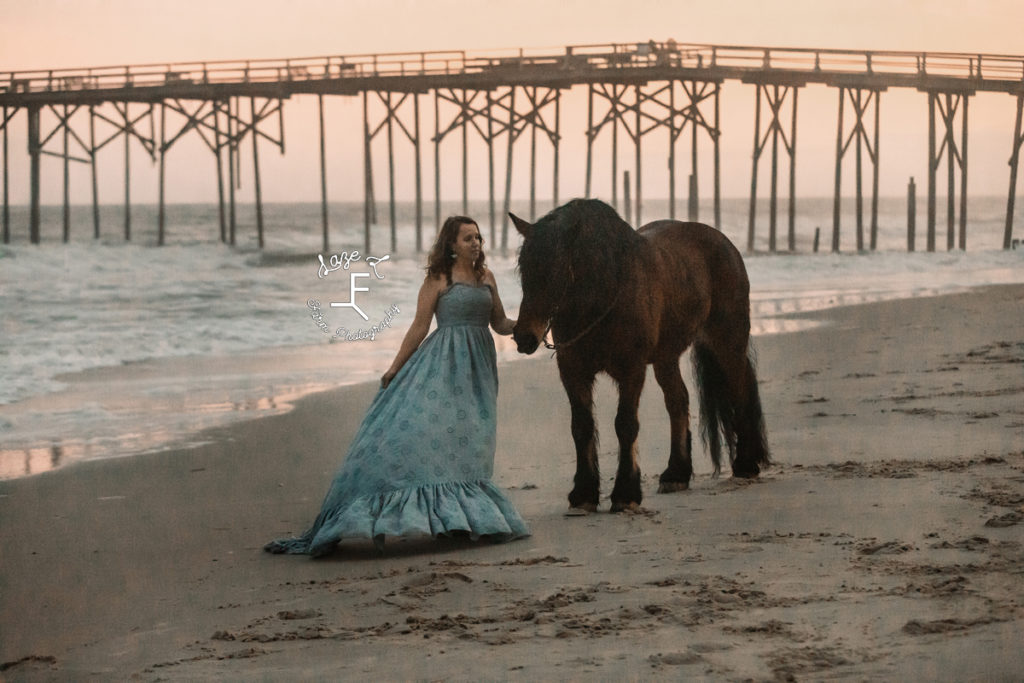 girl in blue dress with horse at sunset on the beach