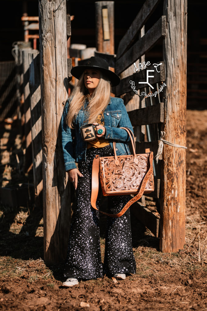 Cowgirl leaning on post with coffee and leather bag