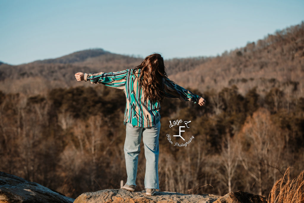 girl standing with arms out facing the mountains