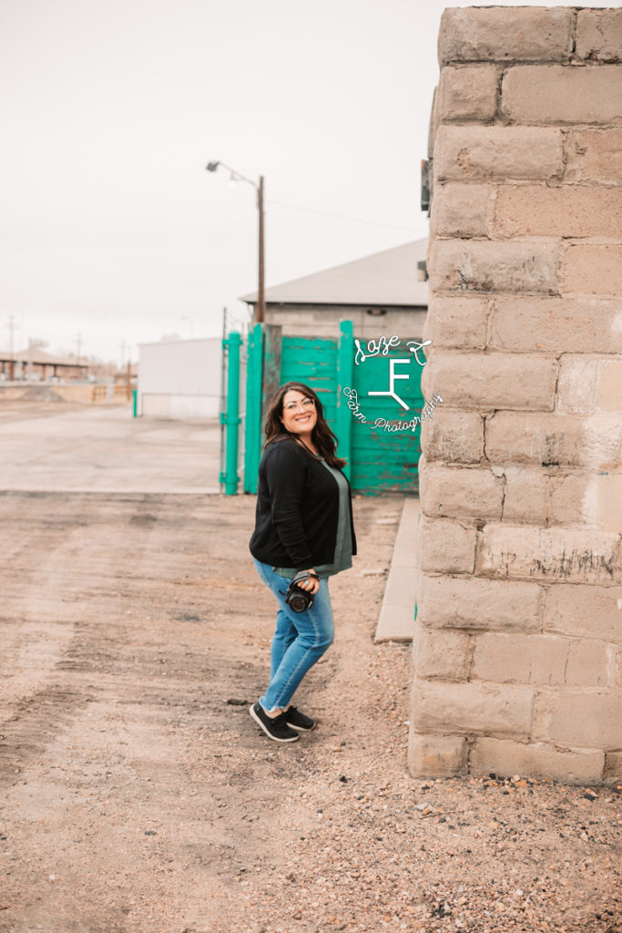 brunette photographer in front of teal fence