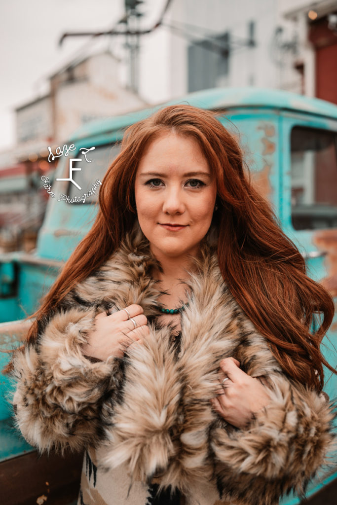 red head in fur coat in front of old truck