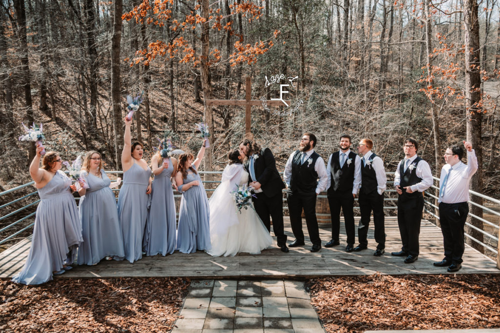 bridal party with bride and groom kissing