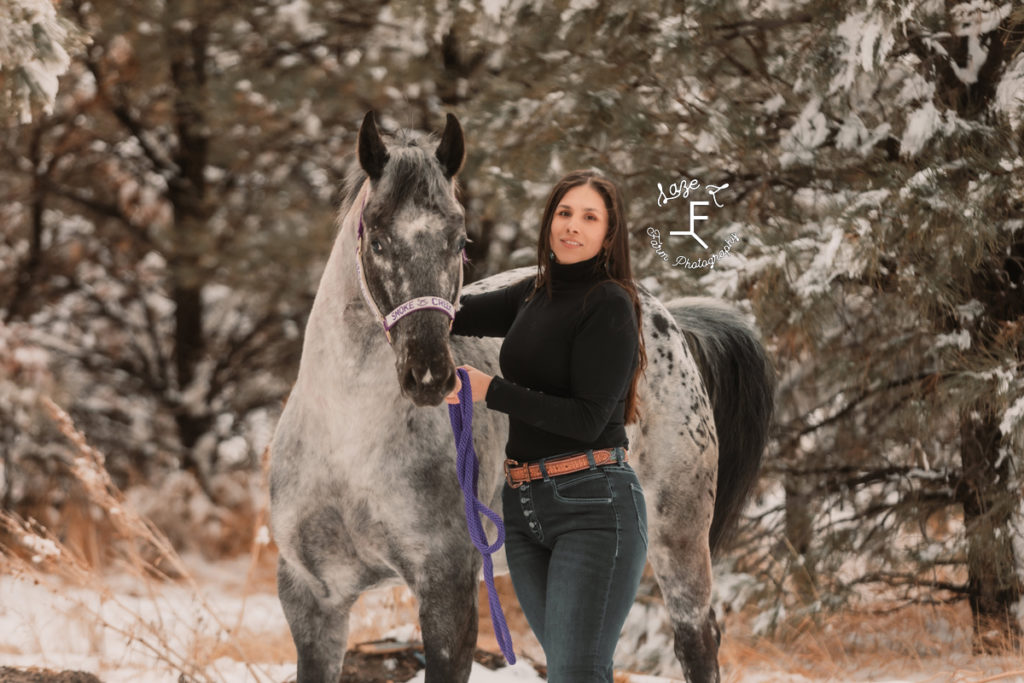 girl with appaloosa horse in front of snow covered trees