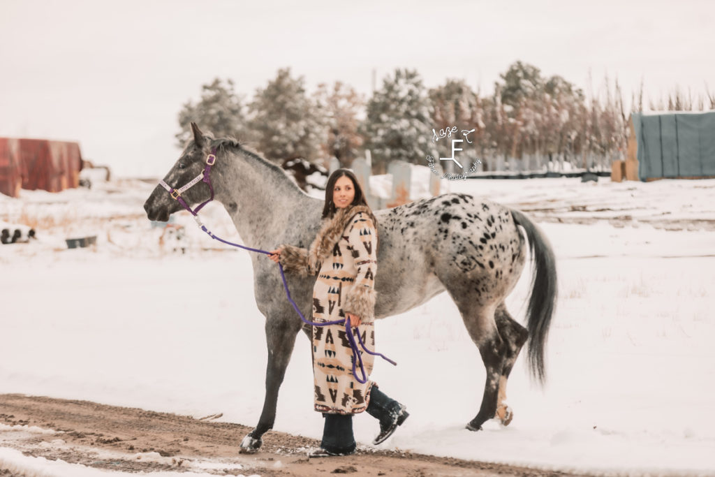 girl in long fur coat with appaloosa in the snow