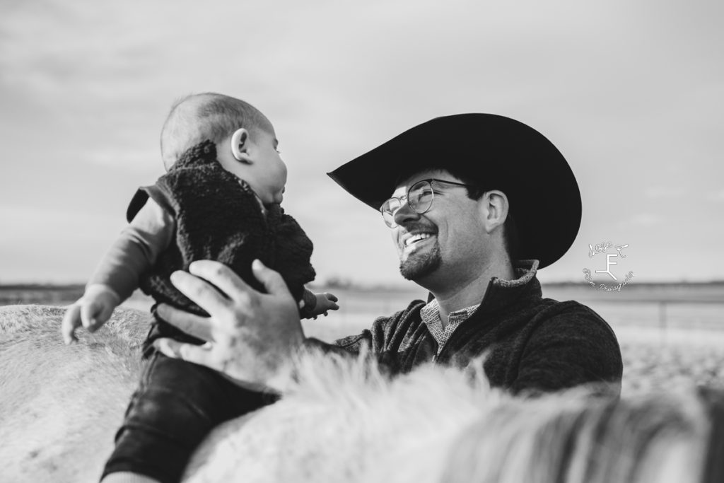 cowboy dad holding son on horse in black and white