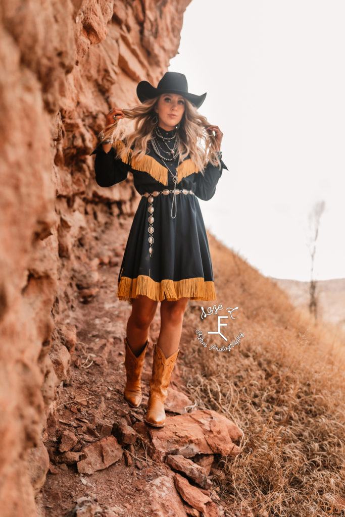 blonde cowgirl in western fringe dress walking beside red rocks