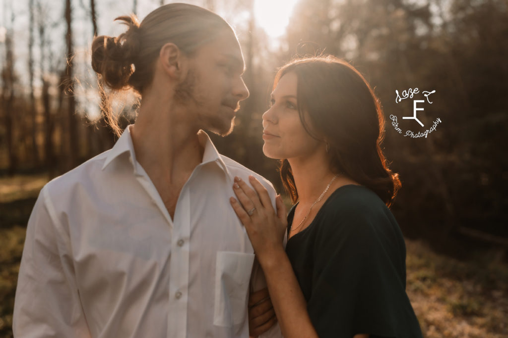 engaged couple looking at each other with sun behind them