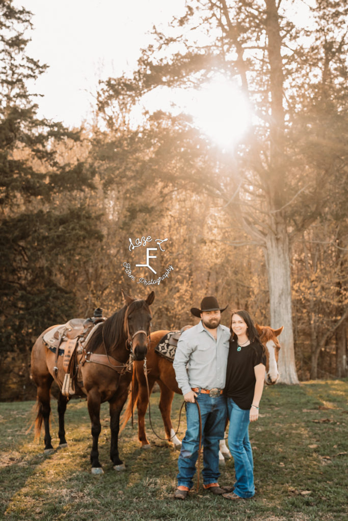 Cowboy and wife with 2 horses with sun behind them