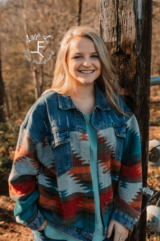 senior girl standing at fence post with Aztec print jacket