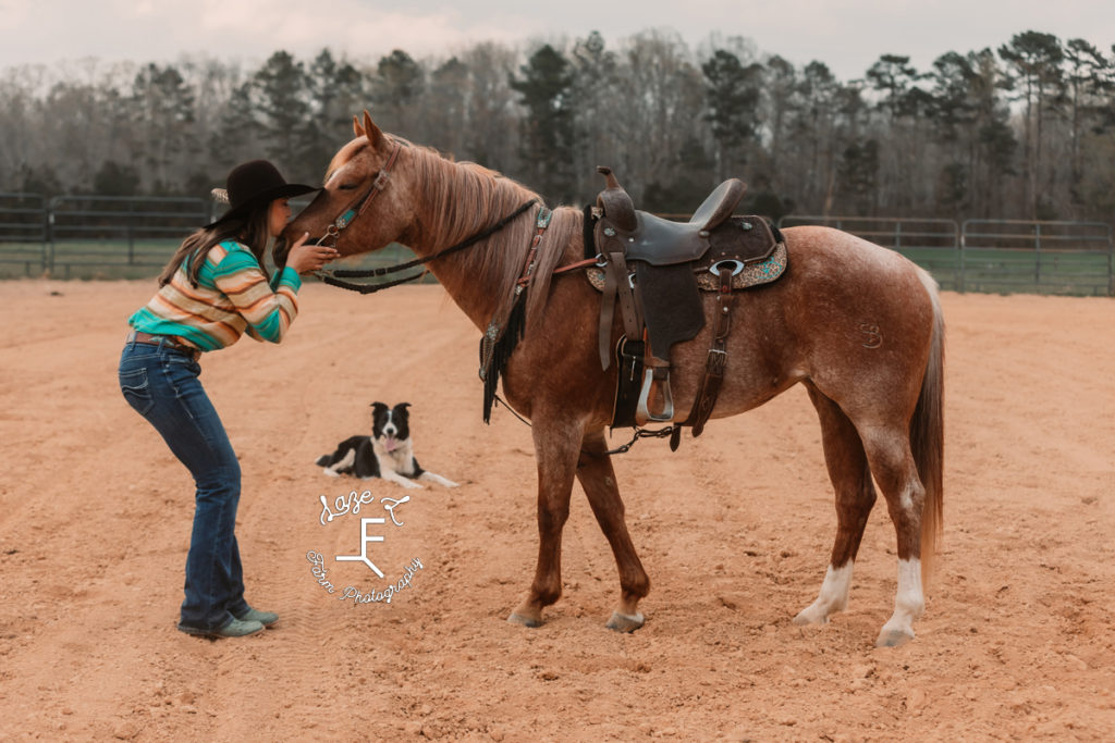 cowgirl kissing horse with dog in background