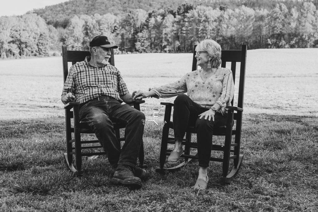 grandparents holding hands in rocking chairs in black and white