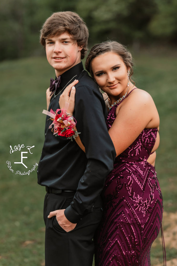 prom couple in purple and black as she is hugging him from behind