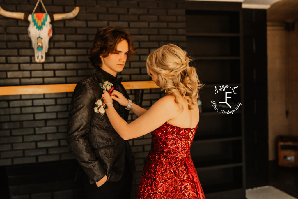 prom couple in red and black as she is pinning his boutonniere