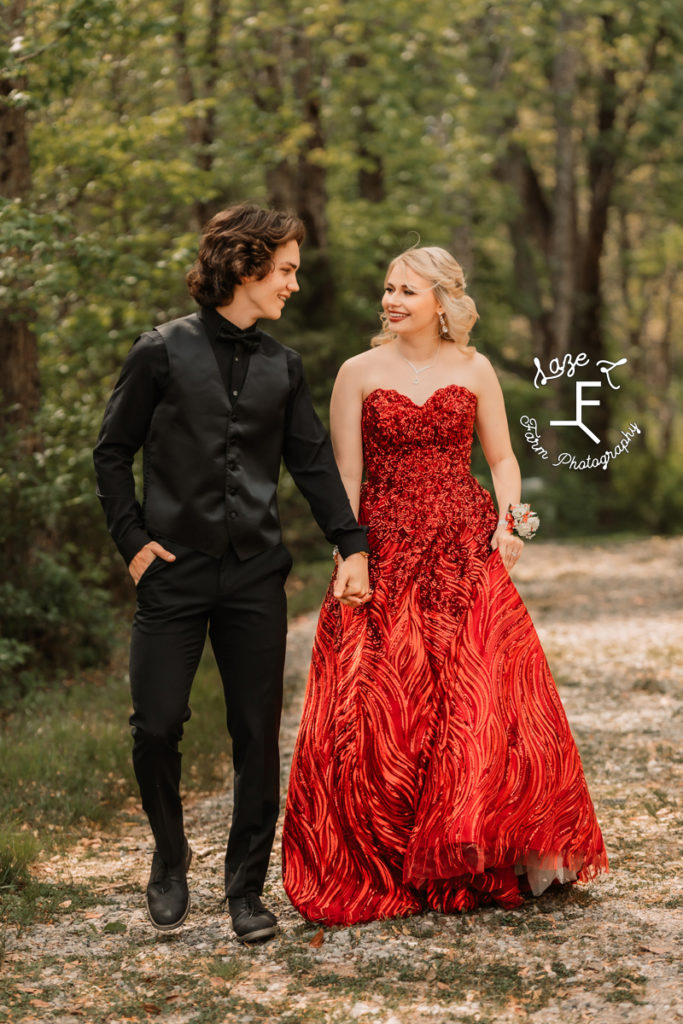 prom couple in red and black walking looking at each other