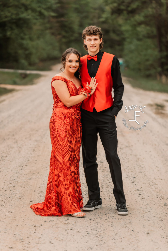 prom couple in orange standing on dirt road