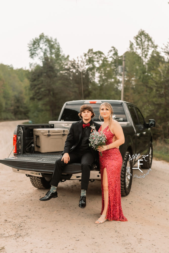 prom couple in red and black sitting on tailgate of truck