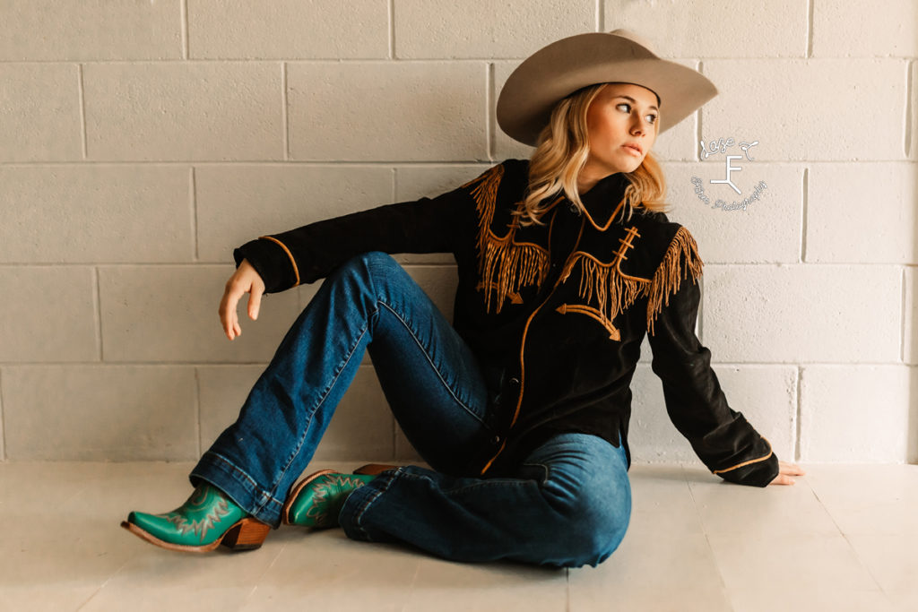 cowgirl in vintage shirt with gold fringe sitting by white wall