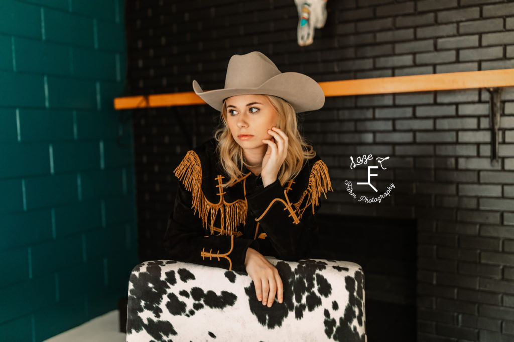 cowgirl in vintage shirt with gold fringe leaning on cow print chair