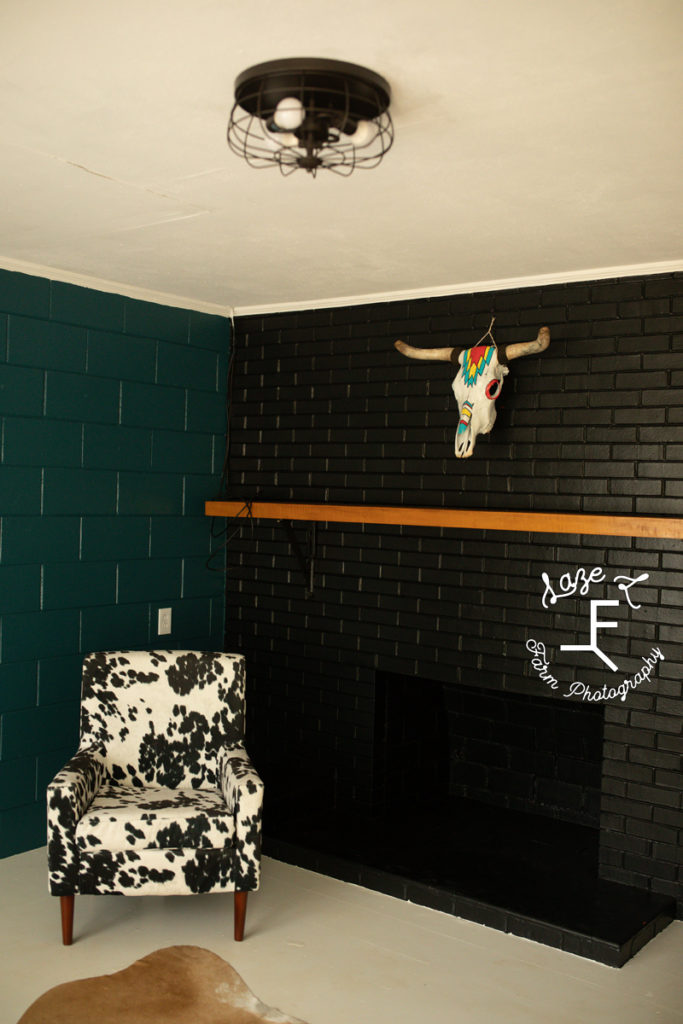teal wall and black fireplace with light wood mantle with cow print chair