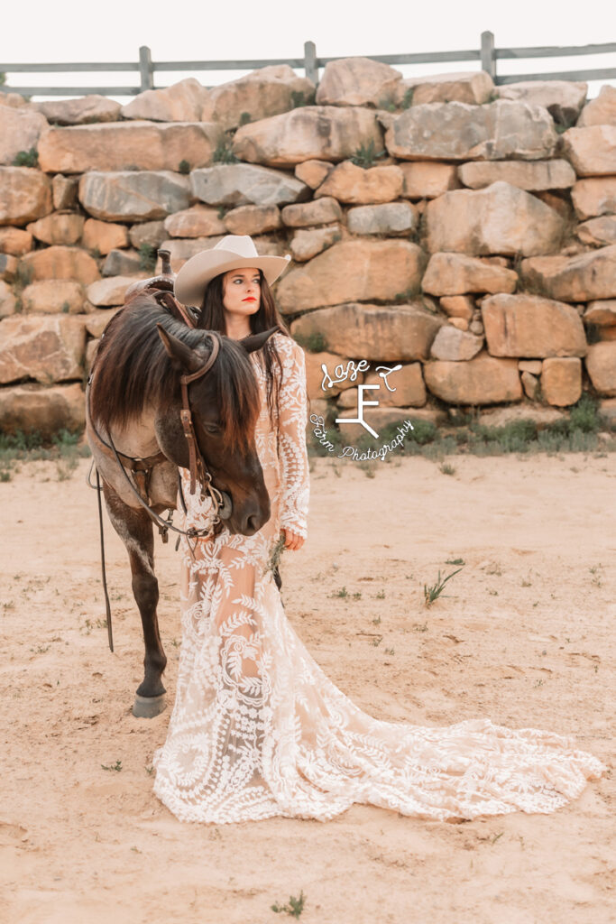 cowgirl standing with horse in lace dress looking left