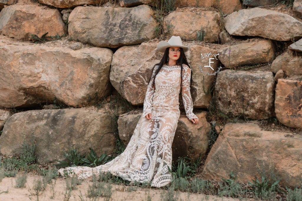 cowgirl in lace wedding dress against rock wall