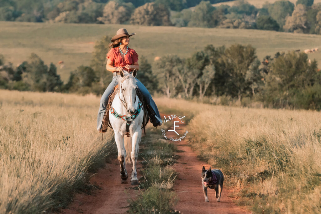 cowgirl riding gray horse with dog beside her