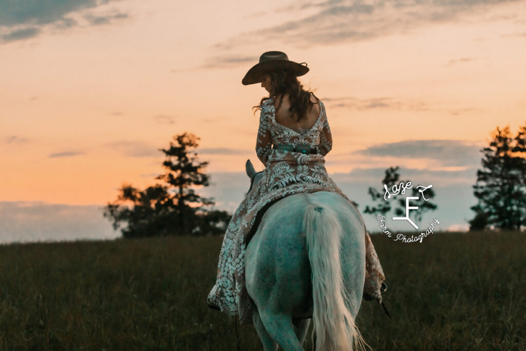 cowgirl riding away at sunset on gray horse in white lace dress