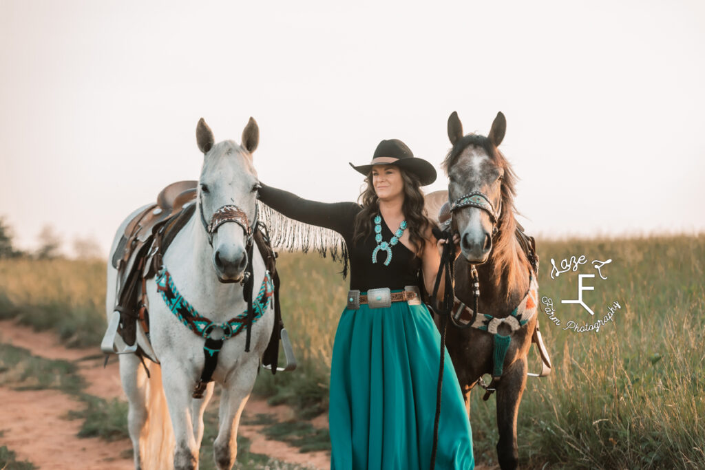 cowgirl with black fringe top with 2 horses