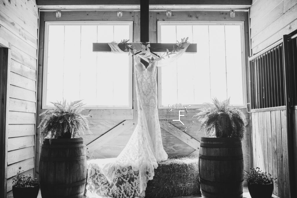 wedding dress hanging from cross in front of barn doors in black and white 