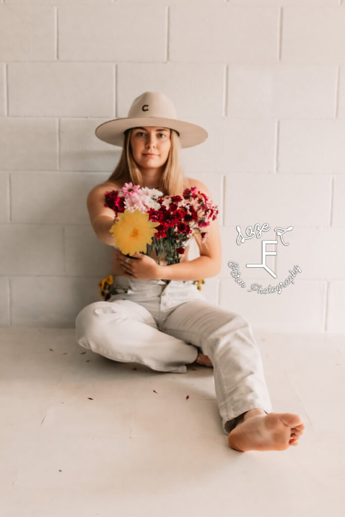 cowgirl sitting with yellow flower pointed at camera