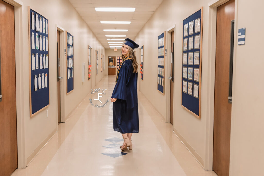 senior girl in cap and gown walking down hall of high school