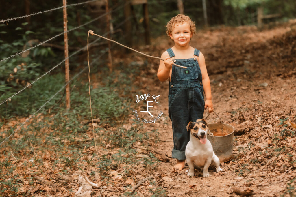 curly headed boy in overalls with fishing pole and dog