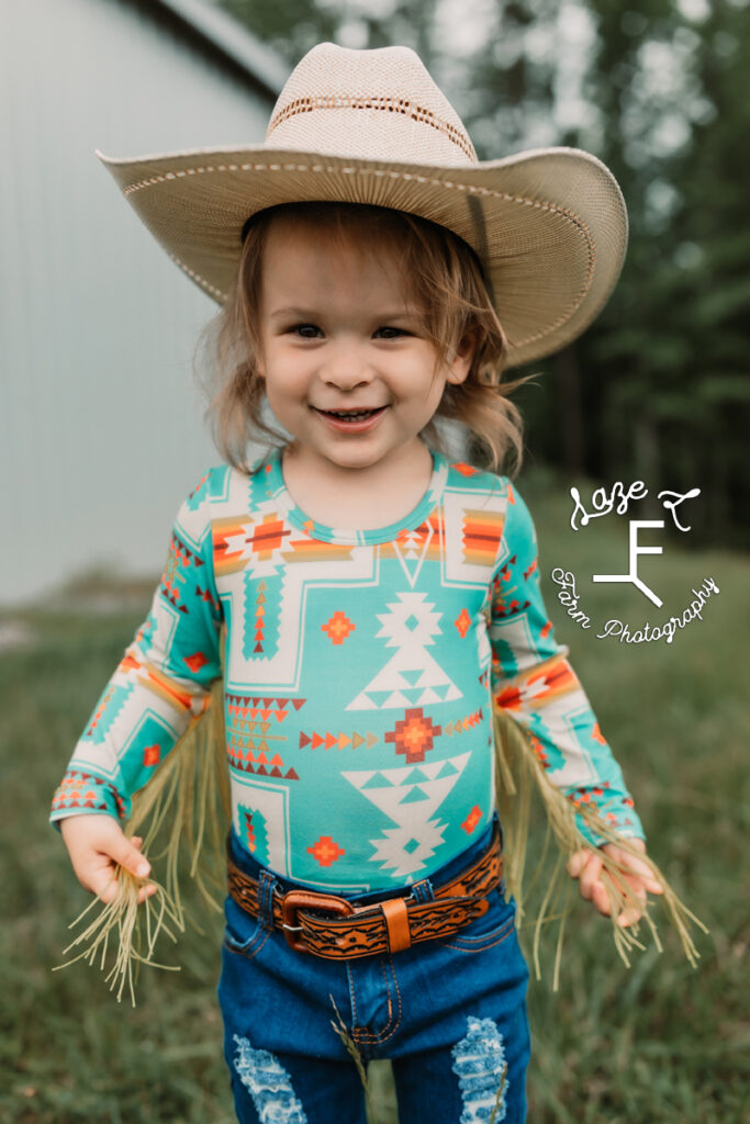 little cowgirl grabbing fringe on her shirt smiling